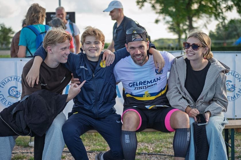 Un finisher avec sa médaille sur un banc entouré d'amis et de famille