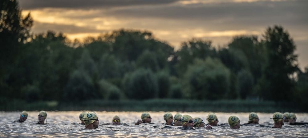 A line of swimmers in green caps in the lake at sunrise